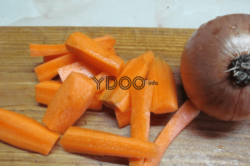 очищенная от кожуры морковь и целая луковица в шелухе на деревянной доске